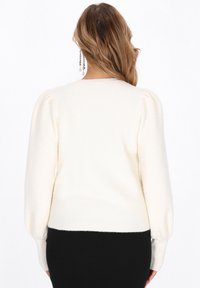 Maglione color crema con maniche a sbuffo, colletto rotondo e orlo rigato. Realizzato in tessuto morbido, presenta una texture liscia e un design minimal.