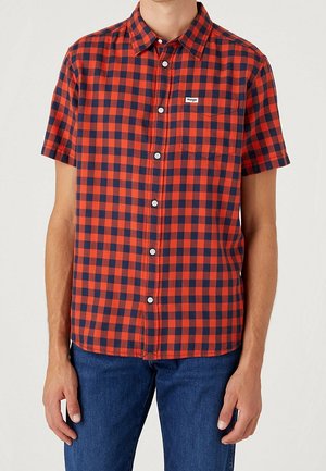 Camisa de manga corta a cuadros rojos y marinos, con cuello tipo button-down, botones en la parte frontal y un pequeño bolsillo en el pecho con una etiqueta de la marca.
