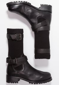 Botas negras hasta el tobillo con cuero texturizado y caña de tela acanalada, que cuentan con una correa con hebilla y una suela de goma gruesa.