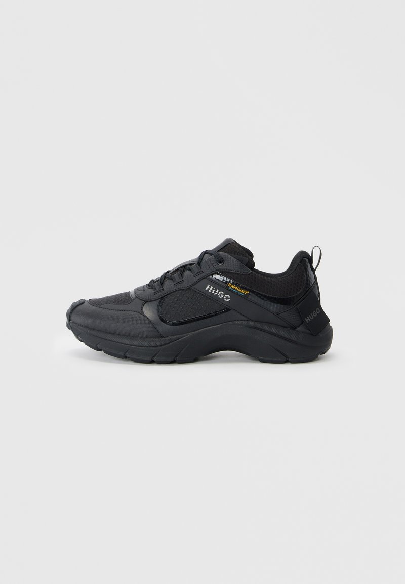 Black athletic shoes featuring a textured upper, padded collar, reinforced toe, and thick sole with a logo accent on the side.