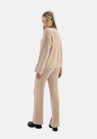 Conjunto de punto acanalado en beige claro, que presenta un suéter de corte holgado con mangas largas y pantalones de pierna ancha a juego, combinados con botas negras gruesas.