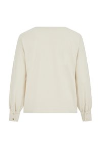 Világos bézs hosszú ujjú felső texturált mintával, széles nyakkivágással és gombos mandzsettával. Egyenes alsó szegély és laza szabás.