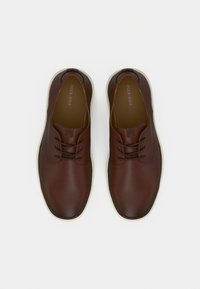 Chaussures décontractées en cuir marron à lacets avec semelles blanches, vues de dessus sur un fond clair uni.