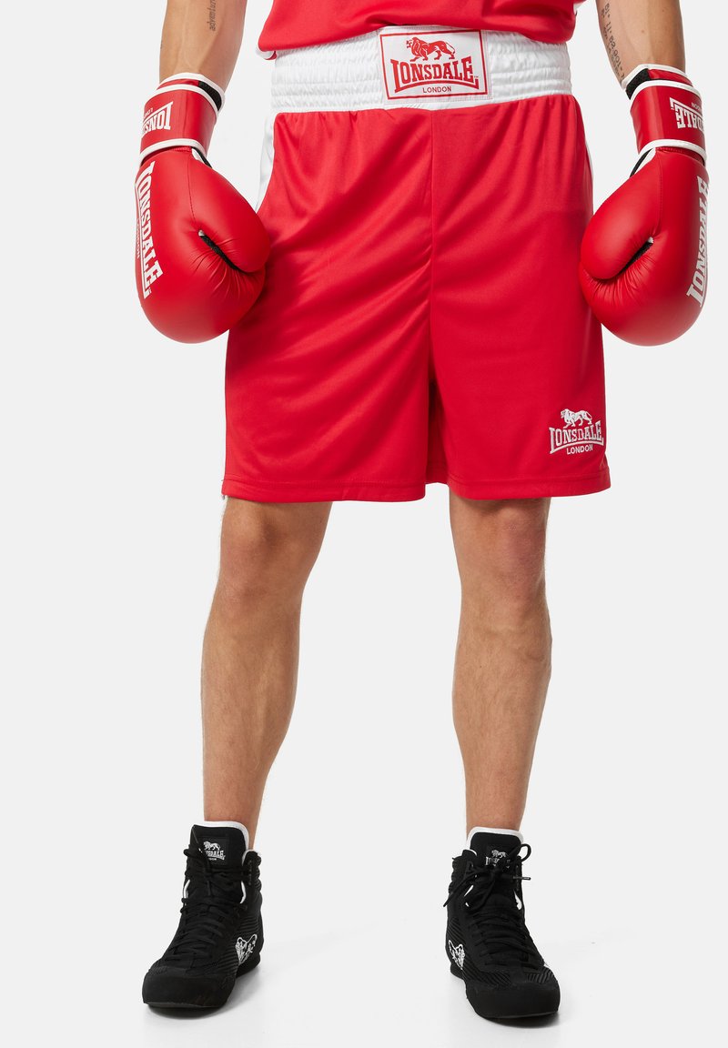 Crvene bokserske šortse s bijelim akcentima, uskog struka, i detaljem s logotipom. Crvene bokserske rukavice s crnim i bijelim akcentima. Crne treniračke tenisice.