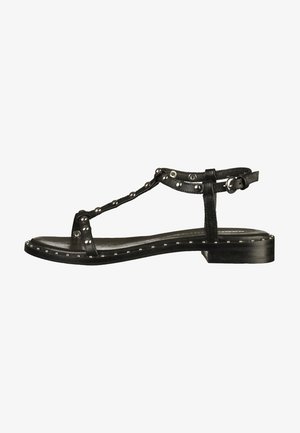 Czarne skórzane sandały z paskiem w kształcie litery T, ozdobione ćwiekami wzdłuż podeszwy, mające płaski obcas i regulowany zamek przy kostce. Gładka tekstura.