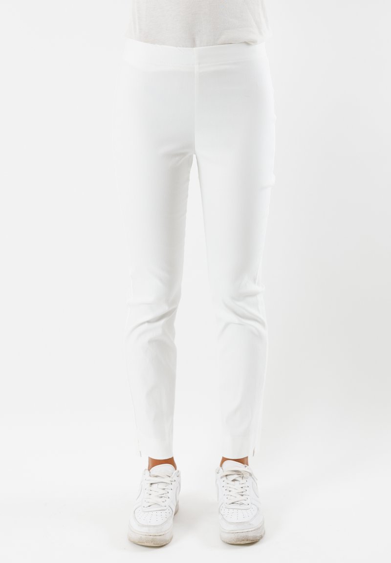 Pantaloni bianchi aderenti realizzati in tessuto elasticizzato, con una finitura liscia. Fessure laterali evidenti alle caviglie. Indossati con sneakers bianche.