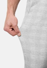 Hellgraue Sporthosen aus strukturiertem Stoff mit einem karierten Muster; eine Hand zieht am Bund, um die Elastizität und Passform zu zeigen.