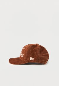 Brown corduroy cap with a curved brim, featuring white embroidered text on the front and a logo accent on the side.