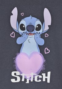 Grafisches T-Shirt mit einem Cartoon-Charakter mit blauer fell, großen Augen und pinken Akzenten, umgeben von Herzen und dem Wort "Stitch" in Weiß.
