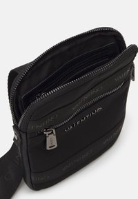 Borsa a tracolla nera in nylon, con chiusura lampo argentata, dettagli di fascia con marchio e più scomparti per l'organizzazione.