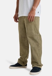 Kaki corduroy bukser med rett passform, teksturert stoff og sidelommer, kombinert med mørkeblå sko og en hvit t-skjorte.