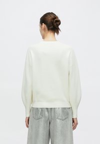 Λευκό φούτερ με λαιμόκοψη, χαλαρή εφαρμογή ώμων, ριμπ μανσέτες και τελείωμα, σε συνδυασμό με ανοιχτό γκρι μεταλλικό παντελόνι με φαρδιά παντελόνια.