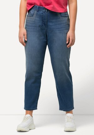 Jeans in denim blu con una vestibilità comoda, caratterizzati da accenti decorativi in strass sulle tasche anteriori e un orlo affusolato. Abbinati a sneakers bianche.
