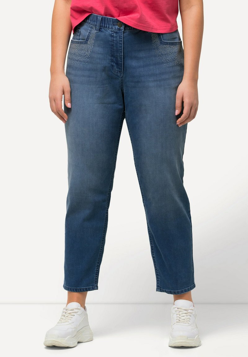 Modré denimové džíny s volným střihem, které mají dekorativní akcenty ze kamínků na předních kapsách a zúžený lem. Doplnené bílými teniskami.