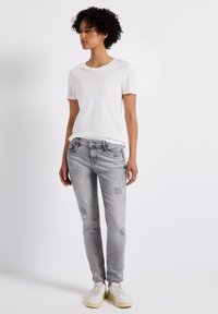 Grijze denim jeans met patch-accenten, gecombineerd met een eenvoudige witte T-shirt met ronde hals. Model draagt witte sportsneakers. Eenvoudig en casual ontwerp.