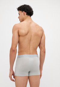 Grå bomullsboxershorts med myk tekstur, med et bredt elastisk midjebånd med lyseblå merkevare, vist fra baksiden.