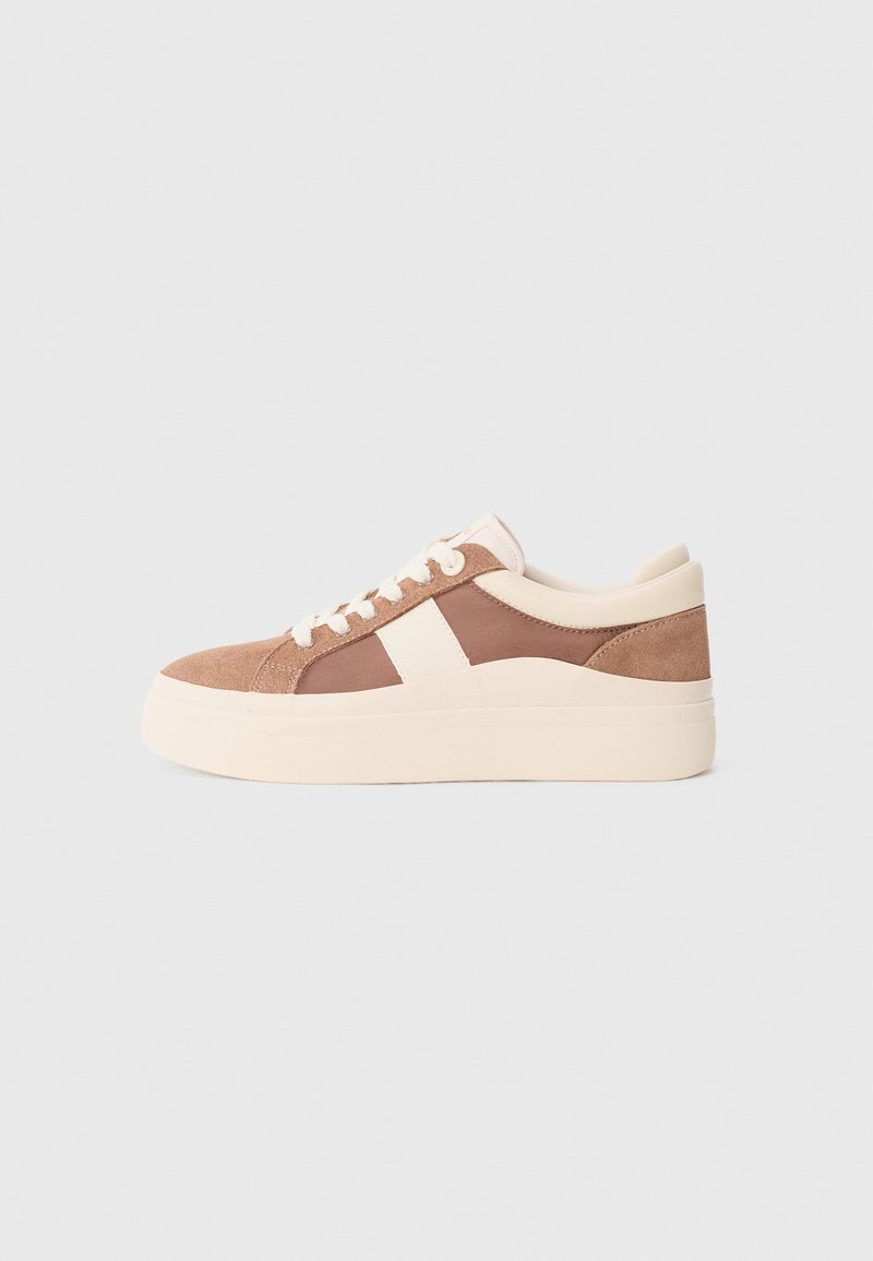 Sneaker in suede marrone con accenti crema, punta rotonda, tomaia testurizzata, lacci piatti e una suola piatta spessa di un beige chiaro.