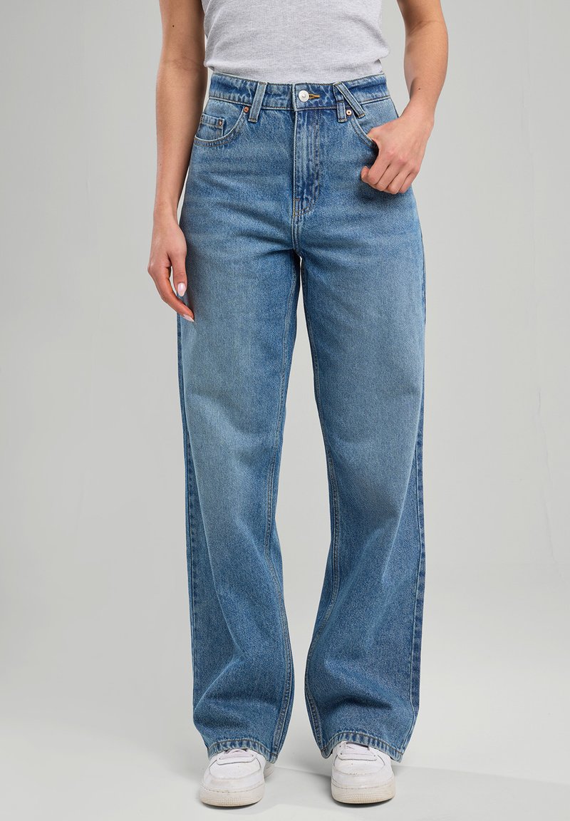 Light blue high-waisted jeans with a wide leg, crafted from denim. Features front pockets and a button fly, paired with white sneakers.