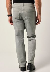 Gråbyxor i texturerad tyg, med två bakfickor och rak passform. Bärs med svarta skor och sedd bakifrån.