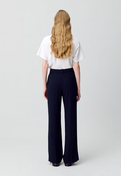 Camisa blanca de manga corta y pantalones anchos azul marino. Los pantalones tienen un tejido liso y estructurado, con una cintura y bolsillos traseros.