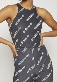 Czarny sportowy top na ramiączkach z białym logo "adidas" oraz wzorem liści. Wykonany z elastycznego materiału, z okrągłym dekoltem i plecakiem.