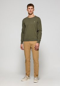 Jersey de punto verde oliva con puños y dobladillo acanalados, combinado con chinos beige y zapatillas de color claro. Detalle de logo bordado simple.