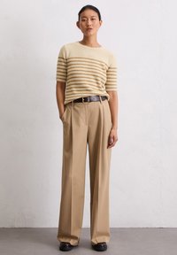 Beżowy sweter z dzianiny z brązowymi, poziomymi paskami, zestawiony z wysokim stanem beżowymi spodniami i czarnym paskiem. Gładkie tekstury, szerokie nogawki.