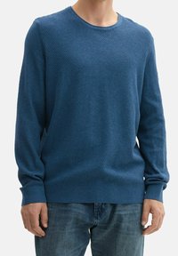 Maglione lavorato a maglia blu con maniche lunghe e collo rotondo. Presenta una superficie testurizzata con una vestibilità rilassata. Abbinato a jeans di denim.