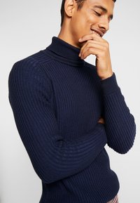Pull à col roulé côtelé marine avec manches longues, tissu texturé, design ajusté et style minimaliste, idéal pour le superposition.