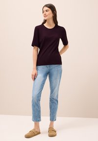 Tmavě fialový top s krátkým rukávem v kombinaci se světle modrými džíny a béžovými nazouvacími botami. Jednoduchý design s kulatým výstřihem a volným střihem.