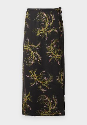 Kvinde med langt mørkt hår iført lyseblå top med V-udskæring og rynkede detaljer, sort blomsterprintet omslagsnederdel og sorte remsandaletter med høje hæle, står med hænderne ned langs siderne.