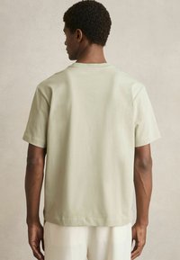 Tricou din bumbac de culoare verde deschis, cu mânecă scurtă și guler tip crew neck, având o croială lejeră și cusături minime, văzut din spate.