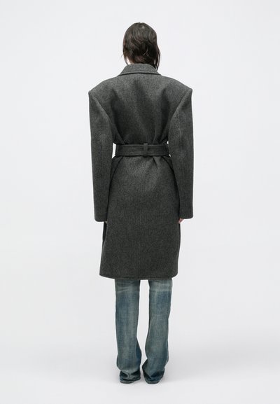 Grå uldfrakke med store skuldre, bælte i taljen og mellemlang længde. Har en hakket krave og blødt, tekstureret stof.