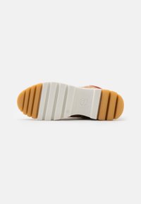 Sneakersål med en tykk, tekstureret gummiytterside. Hvid base med tan og orange accent, der har horisontale riller for bedre greb.