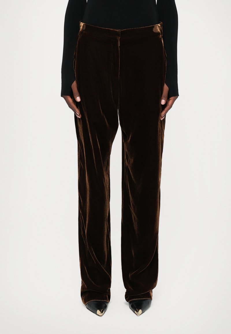 Bordeaux fluwelen wijde broek met een gladde textuur, zijzakken en een knoopsluiting op de taille, gecombineerd met zwarte puntige schoenen.