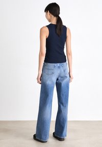 Marinblå ärmlös topp som bärs med ljusblå vida jeans i en urtvättad stil, med två bakfickor och svarta slip-on skor.