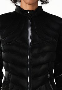 Giubbotto imbottito nero con colletto alto, presenta pattern trapuntati, una cerniera frontale e tasche laterali con dettagli hardware decorativi.