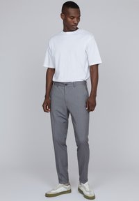 Pantalones rayados grises con un corte ajustado, combinados con una camiseta blanca de manga corta y zapatillas blancas informales con acentos verdes.