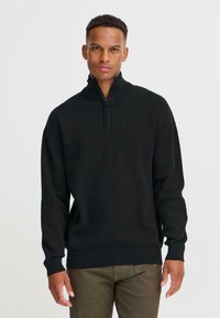 Svart zip-neck genser med lange ermer, ribbestrikkede mansjetter og nederkant; laget av teksturert stoff; minimalistisk design.