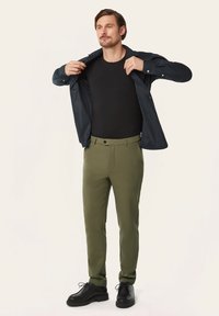 Black t-shirt, dark blue shirt, olive green trousers, and black shoes. Trousers feature a button and a flat front design. Casual outfit.