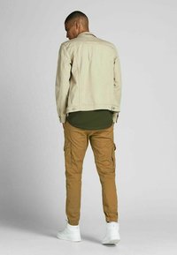 Beige denim jacket, olive green shirt underneath, tan cargo pants, and white sneakers with elastic cuffs; visible stitching and pockets.