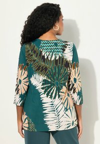 Top en color verde azulado con un patrón floral en blanco, naranja y verde. Presenta mangas de tres cuartos y un escote redondo. Tejido suave y texturizado.