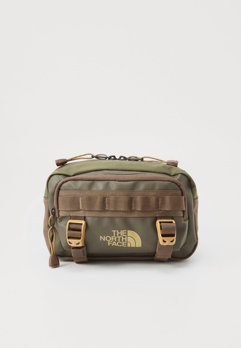 Olijfgroene stoffen tas met bruine accenten, voorzien van twee gouden gespen, een logo-afdruk en een ritsluiting bovenop. Geweven buitenkant.