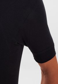 Black short-sleeved shirt showcasing ribbed texture, fitted design, and a clean finish at the sleeve cuffs. Smooth fabric with no visible patterns.