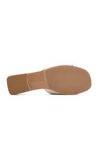 Beige hoge hakken met een gladde bovenkant en een getextureerde rubberen zool. De zool heeft horizontale groeven voor betere grip.