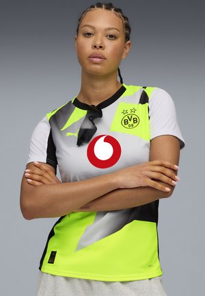 Het sporttrui met korte mouwen heeft blokken in zwart, grijs en neon groen, met een groot rood cirkellogo en een clubembleem op de borst.