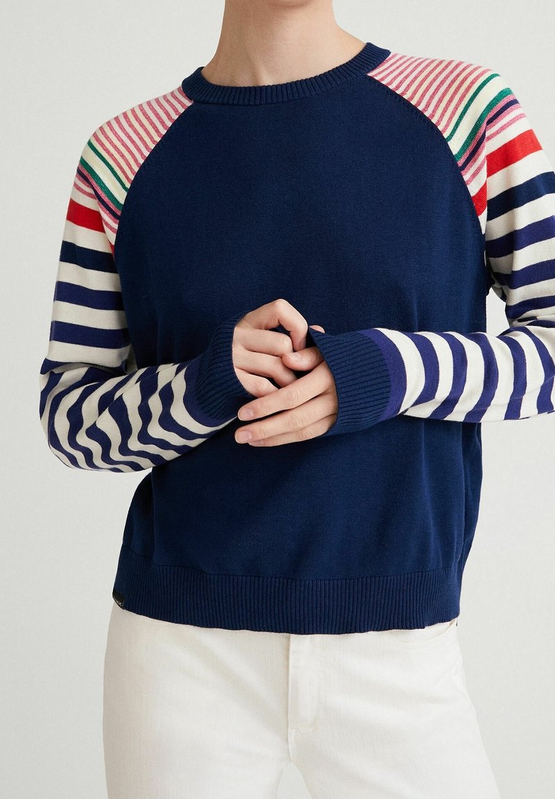 Marineblauwe trui met contrasterende gestreepte mouwen in rood, groen en wit. Voorzien van geribbelde manchetten en zoom, lichtgewicht gebreide textuur.