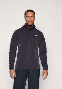 Veste extérieure noire avec fermeture éclair sur le devant, capuche et accents orange. Comprend un tissus texturé et une coupe ajustée, adaptée aux activités sportives.