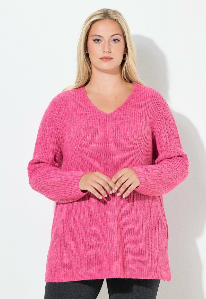 Rosa gestrickter Pullover mit V-Ausschnitt, geripptem Muster, langen Ärmeln und legerer Passform, kombiniert mit schwarzen Leggings.