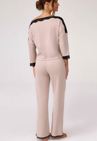 Zestaw piżamowy w miękkim różowym materiale z czarnymi koronkowymi akcentami. Posiada luźną bluzkę i spodnie o prostych nogawkach, podkreślając swobodny styl.